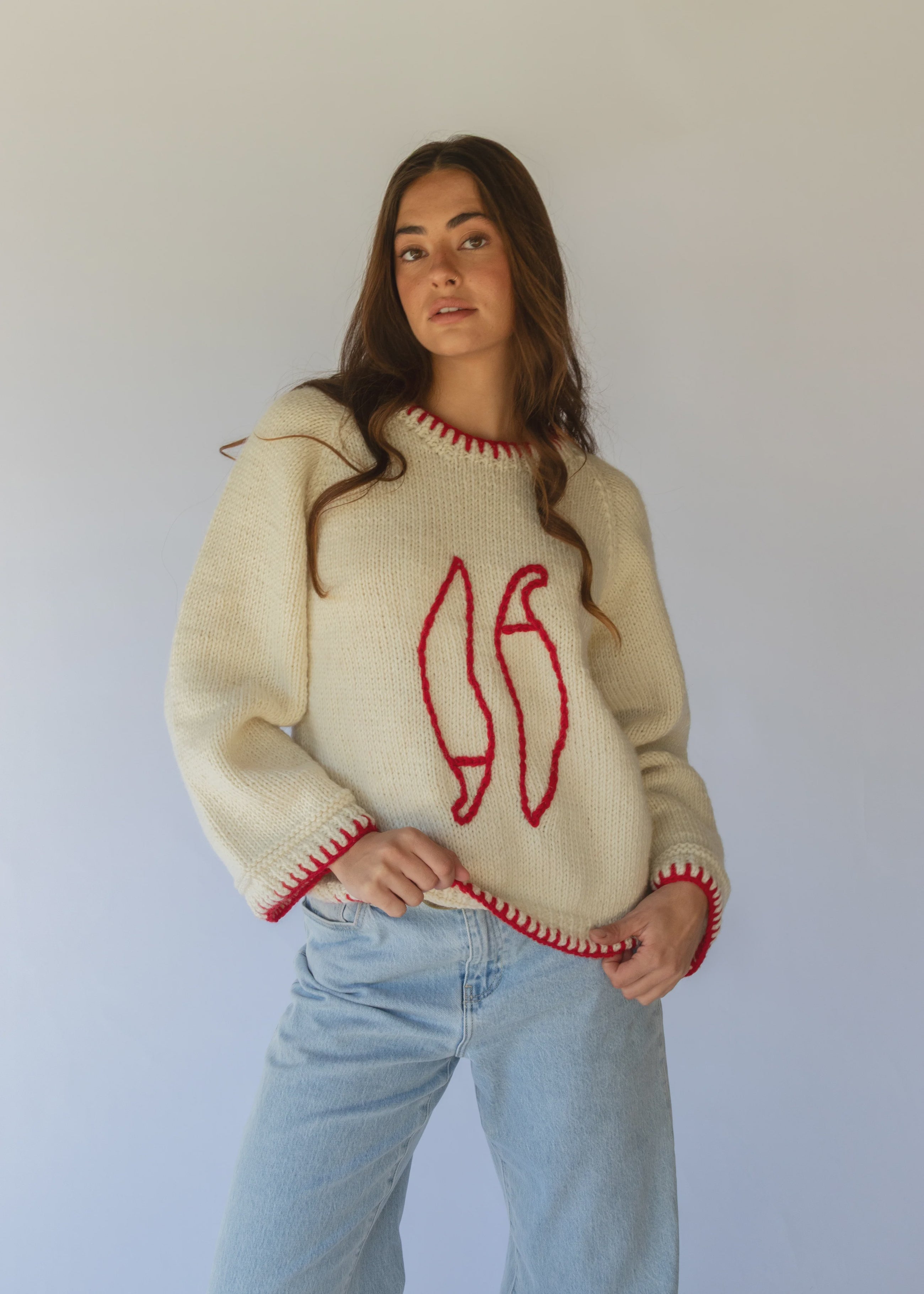 HOBO AND HATCH | Sol Sweater - Chilli - Hand-knitted cream wool sweater crafted from 100% New Zealand wool, featuring playful embroidered chilli motifs and contrasting red blanket-stitch detailing along the hem, neckline, and sleeves. Designed with a relaxed fit, round neckline, and open sleeves for effortless layering or standalone wear. Ethically handcrafted in Nepal alongside local artisans.