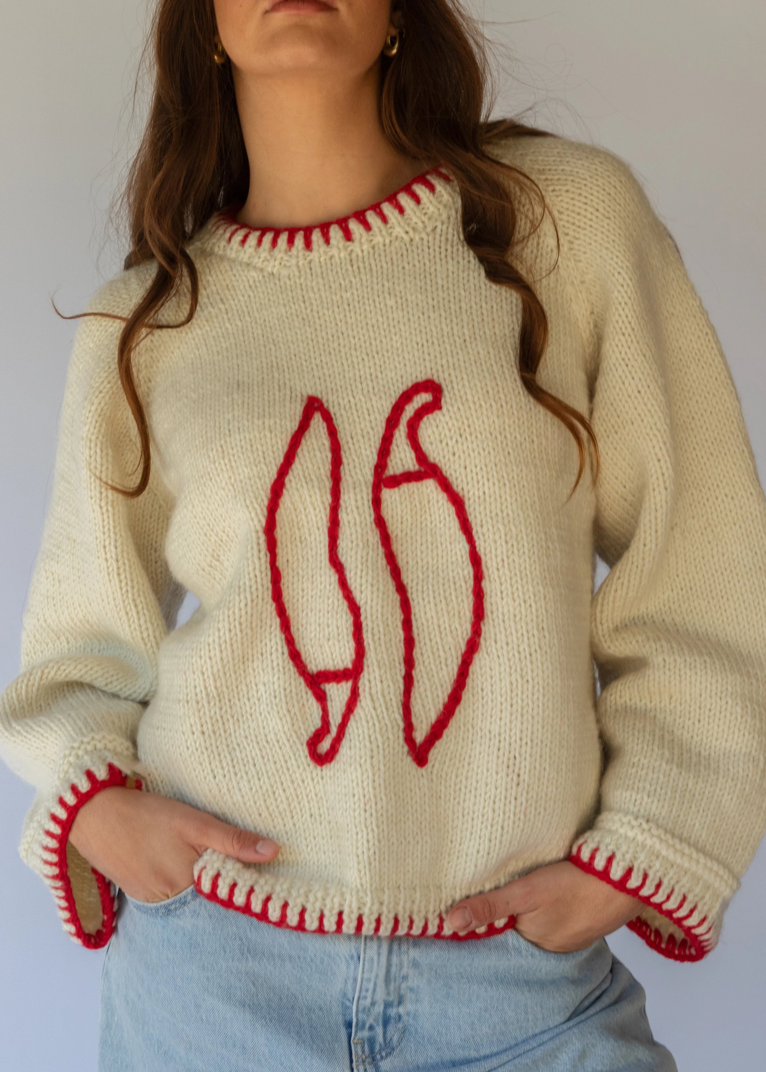 HOBO AND HATCH | Sol Sweater - Chilli - Hand-knitted cream wool sweater crafted from 100% New Zealand wool, featuring playful embroidered chilli motifs and contrasting red blanket-stitch detailing along the hem, neckline, and sleeves. Designed with a relaxed fit, round neckline, and open sleeves for effortless layering or standalone wear. Ethically handcrafted in Nepal alongside local artisans.