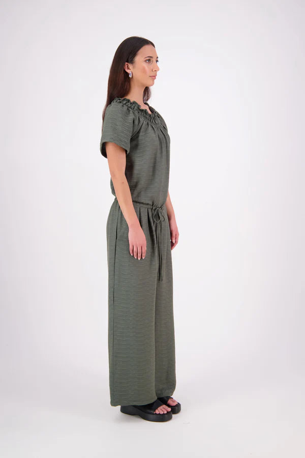 The N-E-S Muses Jumpsuit features a shirred off-the-shoulder top with cap sleeves, an elasticated back waist, and a self-drawcord front for a flattering, adjustable fit. The lower half mirrors the relaxed fit of our Lounge Jumpsuit, with angled seams, centre front detailing, and practical front pockets
